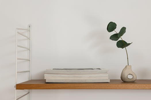 A wooden shelf with a unique ceramic vase and stacked magazines against a white wall.